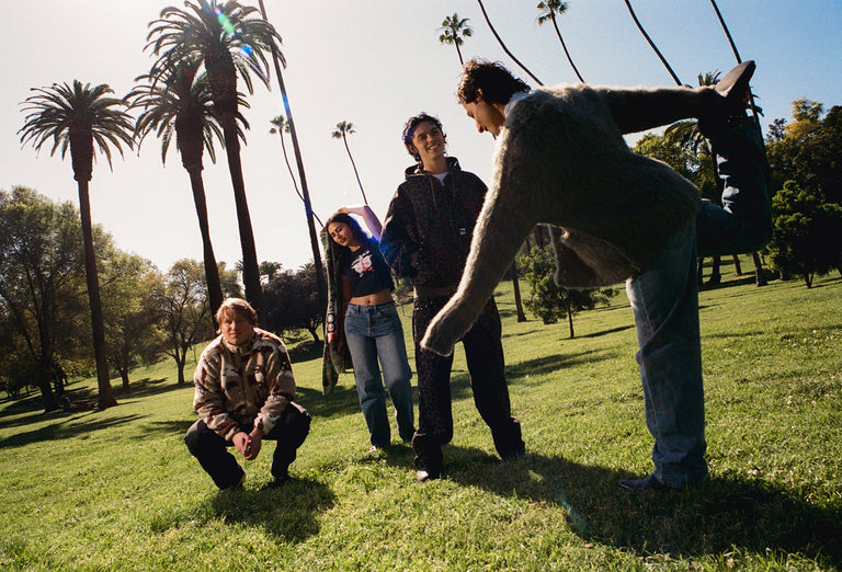 four individuals standing in a grassy field with palm trees behind them
