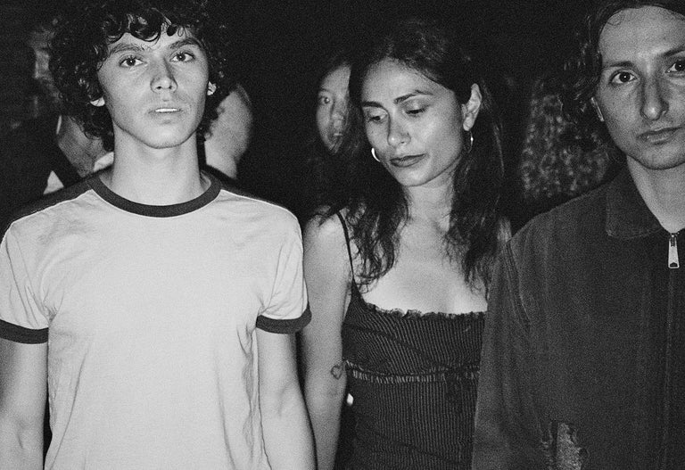 Black and white photo of three people standing together against a dark background