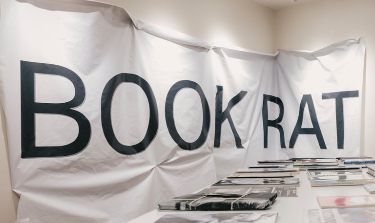 Large white banner with 'BOOK RAT' printed on it, displayed in a room with books.