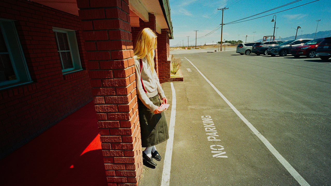 Person standing on a sidewalk next to a building with a no parking sign on the street.