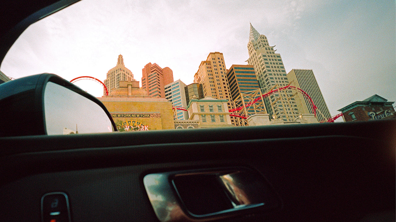 Cityscape view from inside a car with tall buildings and a roller coaster.