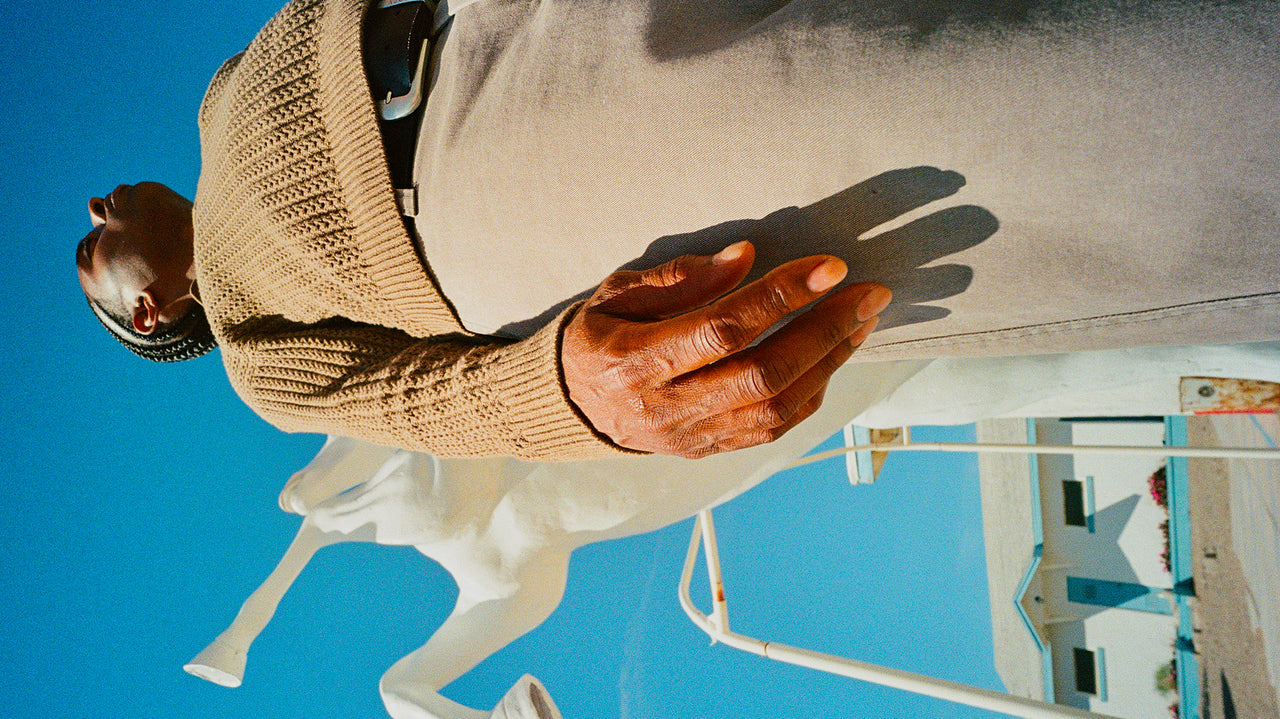 Person wearing a beige sweater standing next to a white horse statue against a blue sky.