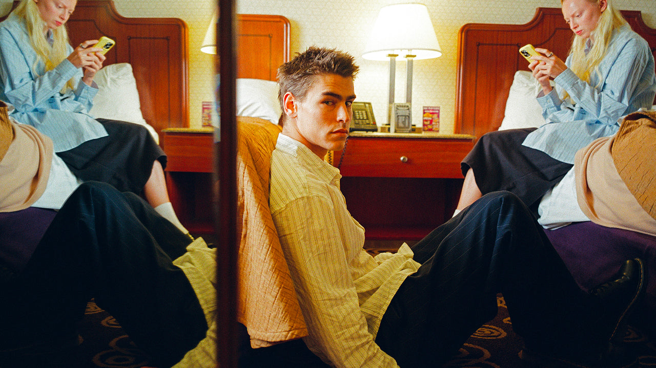 Two people sitting on a bed in a room with a mirror reflecting their image.