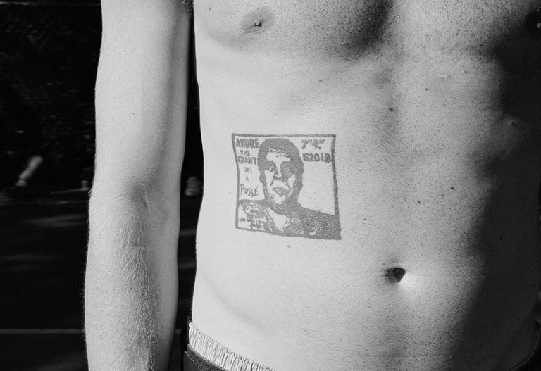Man with a tattoo of a portrait on his stomach, wearing dark pants.