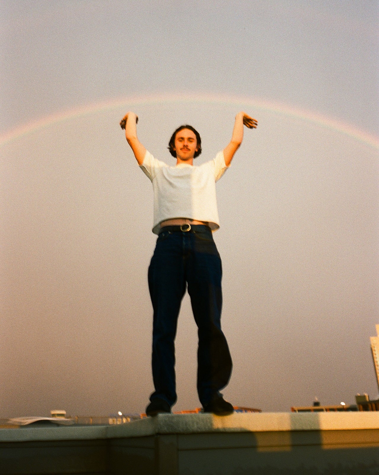 Person standing on a ledge with a rainbow in the sky