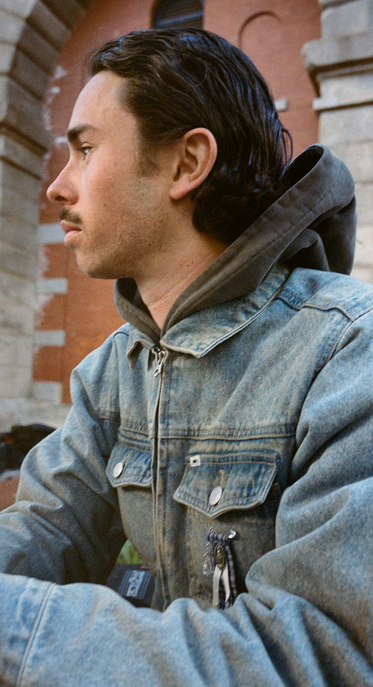 Man wearing a denim jacket with a brick building in the background