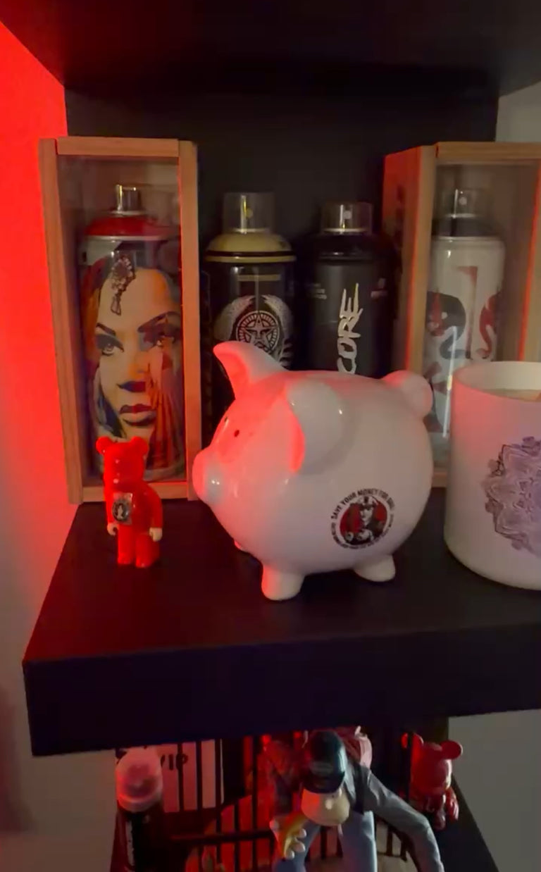 Piggy bank with a logo on a shelf with various items including spray cans and figurines.
