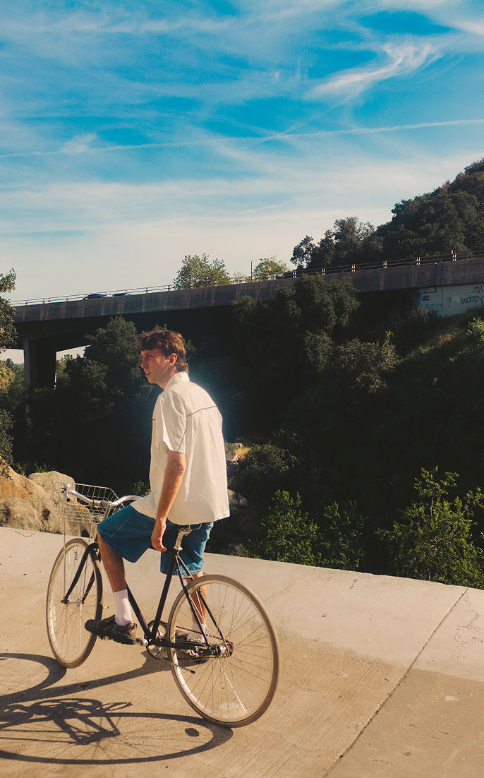 Person riding a bicycle on a concrete ledge with a scenic background of trees and a bridge.
