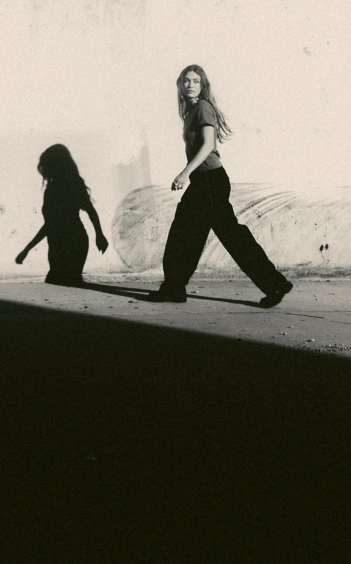 Two people walking on a sidewalk with their shadows cast on the ground.