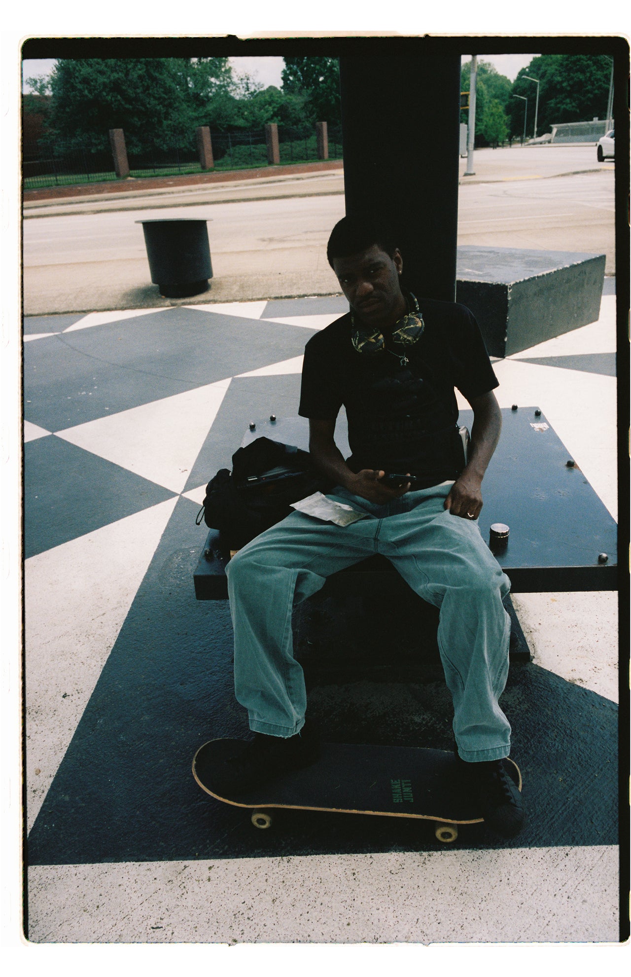 Person sitting on a skateboard with a black shirt and light blue jeans in an outdoor setting.