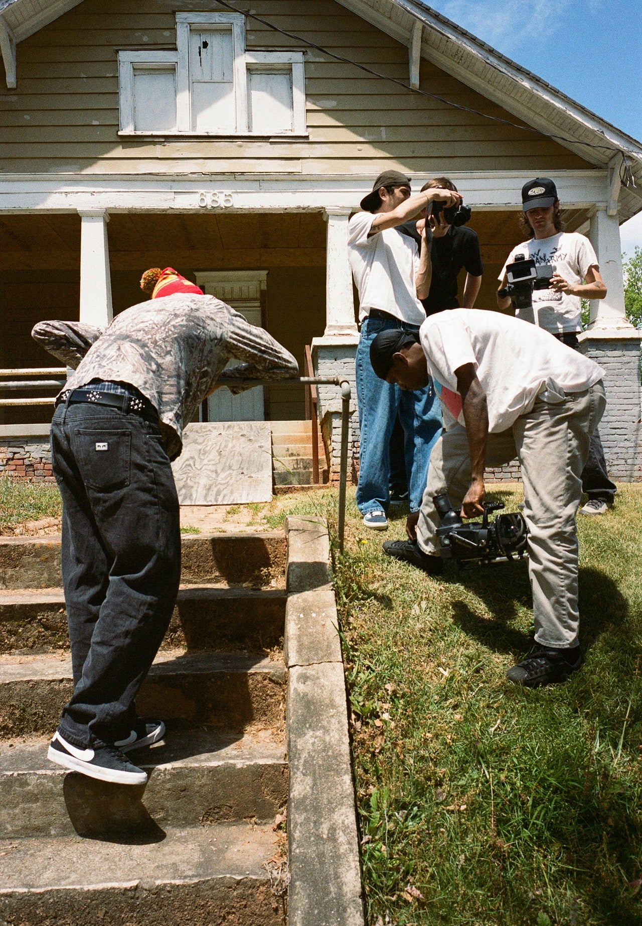 Group of people filming a skate trick outside a house.