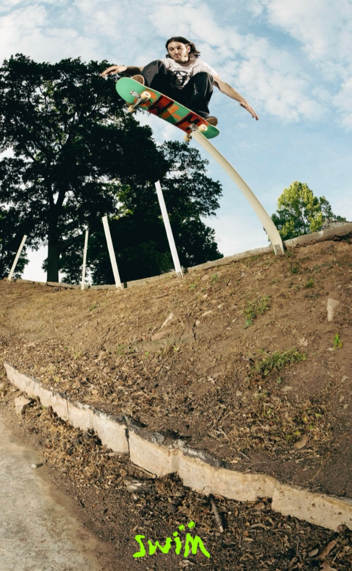 Person skateboarding on a dirt ramp with trees and a clear sky in the background