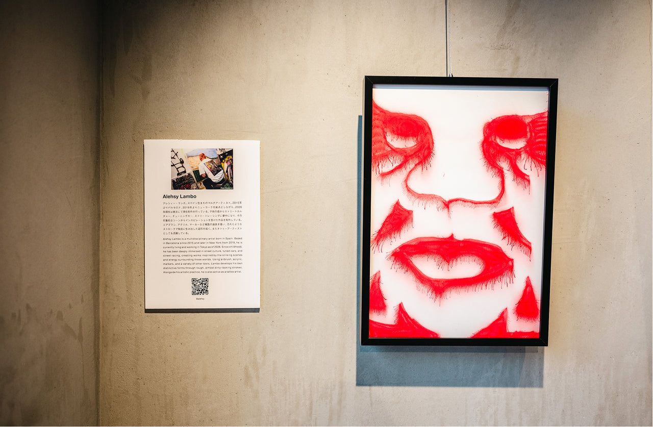 Framed artwork of a face with red accents on a textured wall next to a poster.