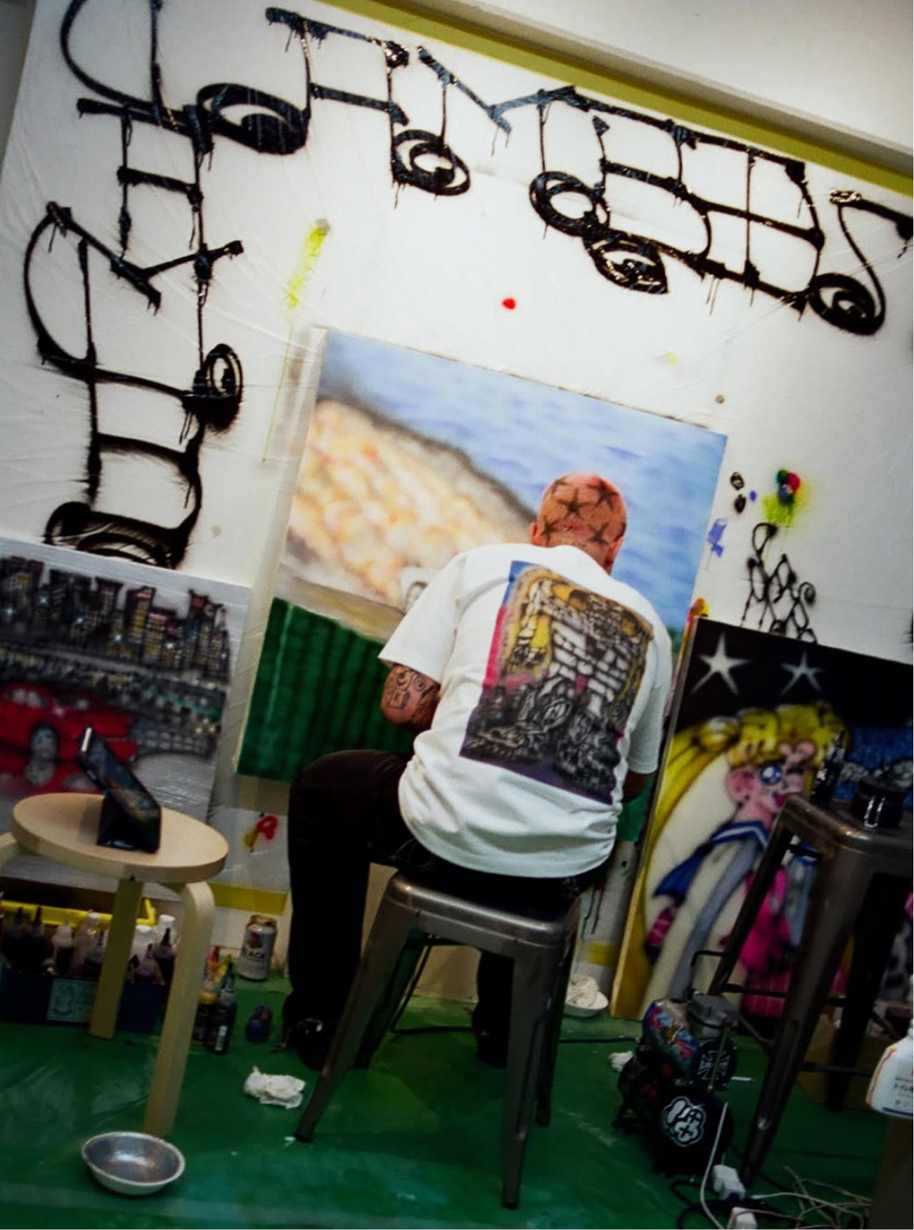Person sitting on a stool in an art studio with various artworks and tools around