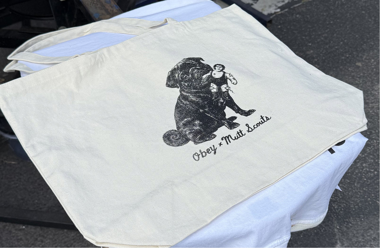 Beige tote bag with a black dog illustration and 'Obey' text on a white shirt.